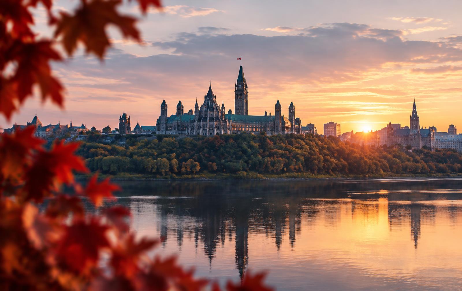 Parliament Hill in Ottawa at sunrise, framed by red maple leaves
